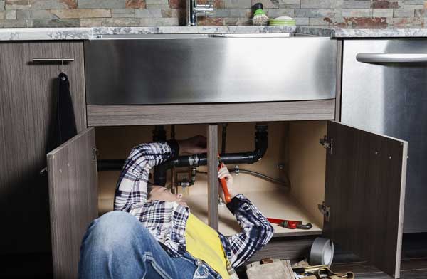 A plumber fixing pipes under a kitchen sink.