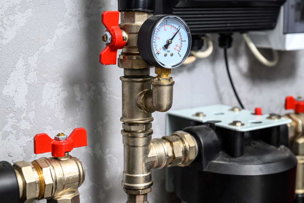 Close-up of a pressure gauge on brass plumbing with red valve handles.