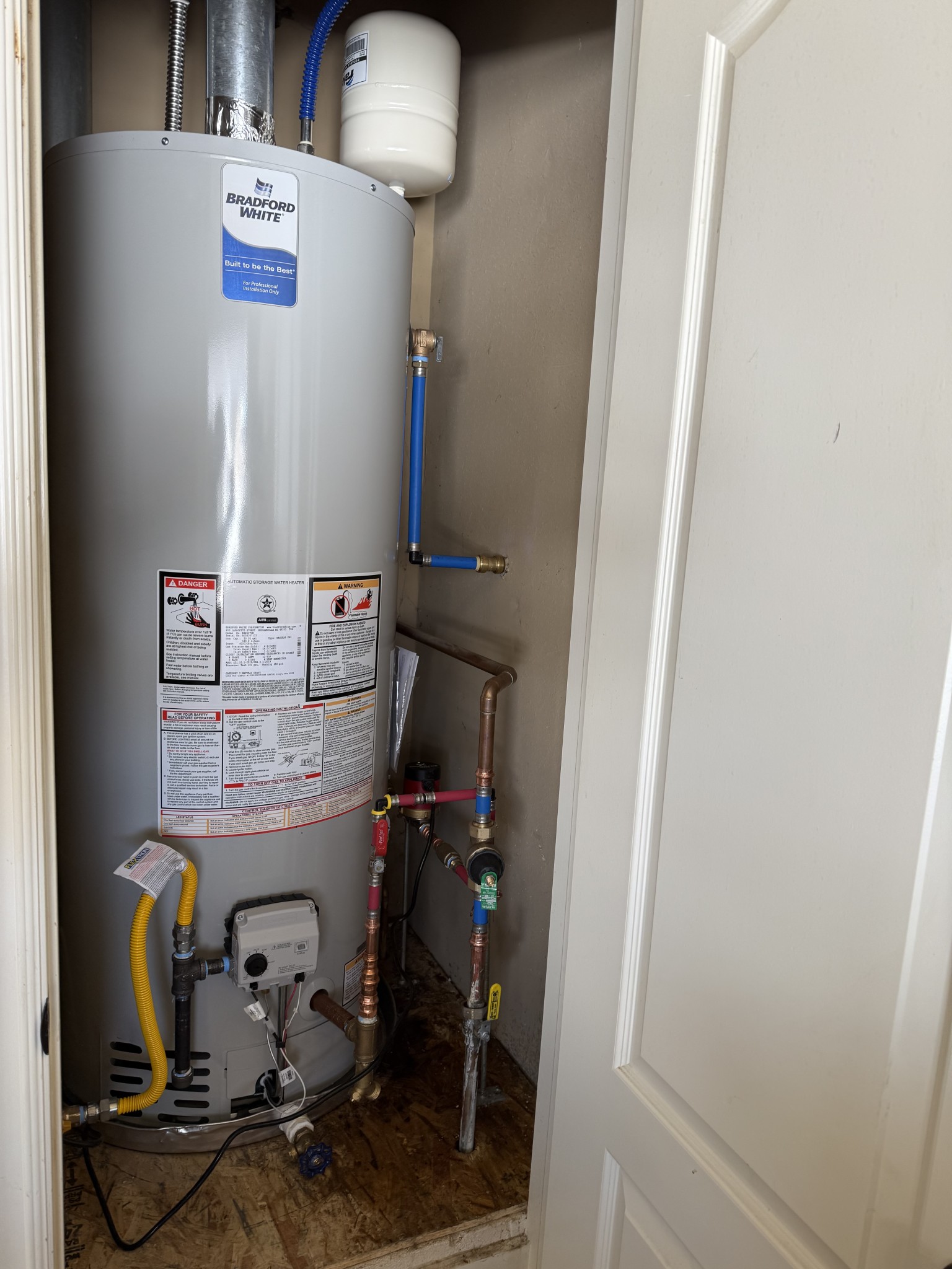 A water heater installed in a utility closet with pipes and labels.