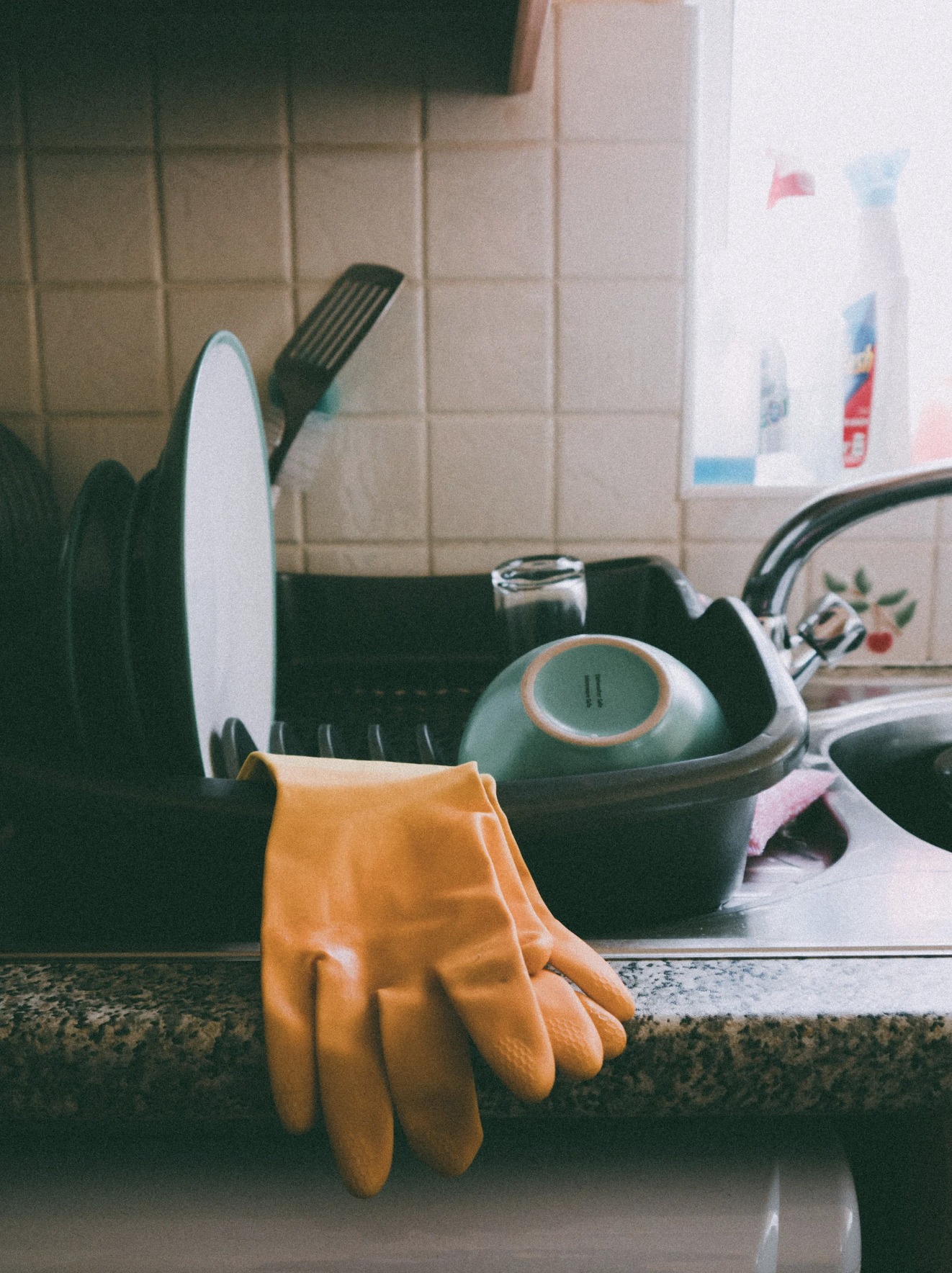 Kitchen sink filled with dishes and gloves hanging on the edge.