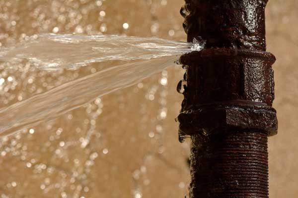 Water flowing forcefully from a rusty pipe against a blurred background.
