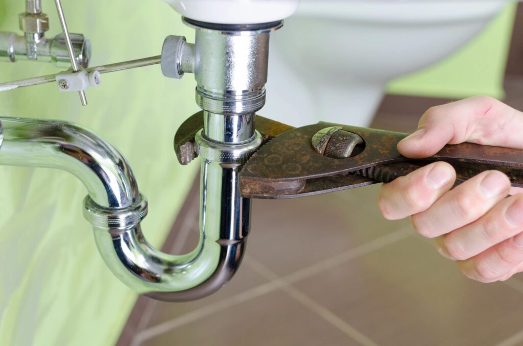 A person fixing a sink pipe with a wrench.